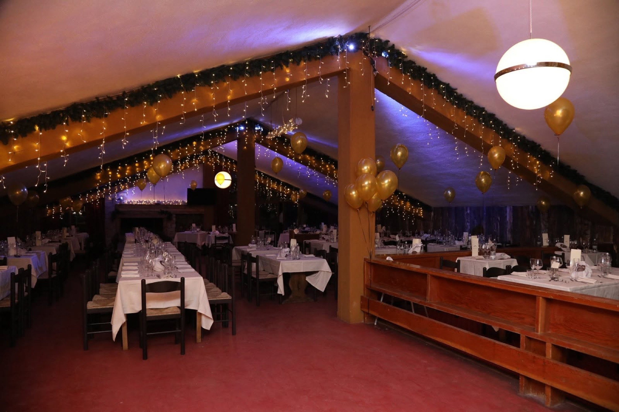La sala allestita per il Capodanno con tavoli apparecchiati, luci a cascata e palloncini dorati